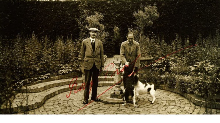 An archive photograph of two people standing in a garden, one with two dogs